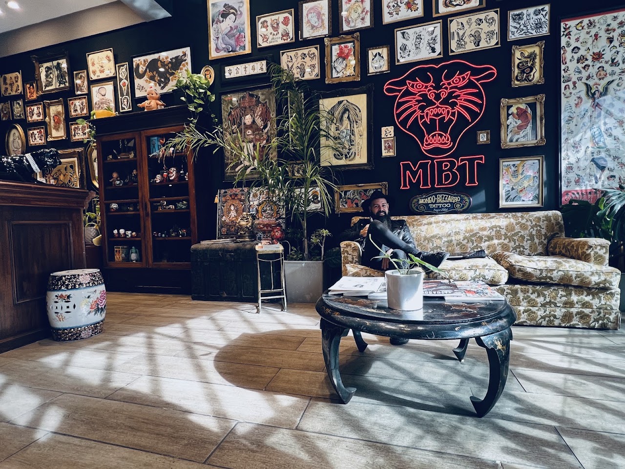 Interior del estudio Mondo Bizarro Tattoo, con paredes negras cubiertas de flash art enmarcado y el neón MBT